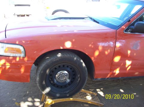 2002 Ford Crown Victoria - The photo shows the front driver's side of an orange sedan, with the wheel resting on a yellow ramp.