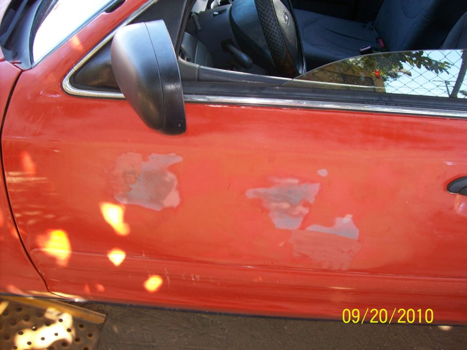 Red car door with peeling paint and black side mirror. 2002 Ford Crown Victoria