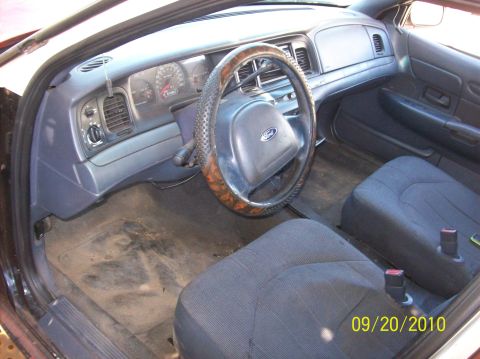 2002 Ford Crown Victoria - The interior of a Ford Crown Victoria shows wear and tear, with a dirty floor and a steering wheel cover.