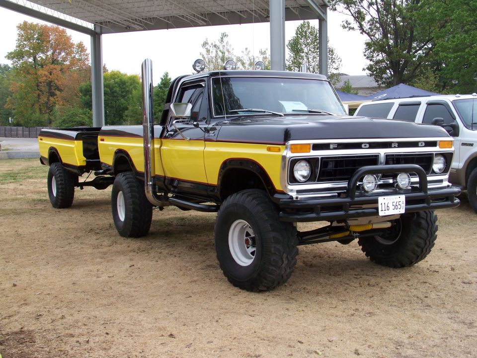 Lifted black and yellow Ford pickup truck towing a yellow trailer. It has large tires and a tall exhaust pipe
