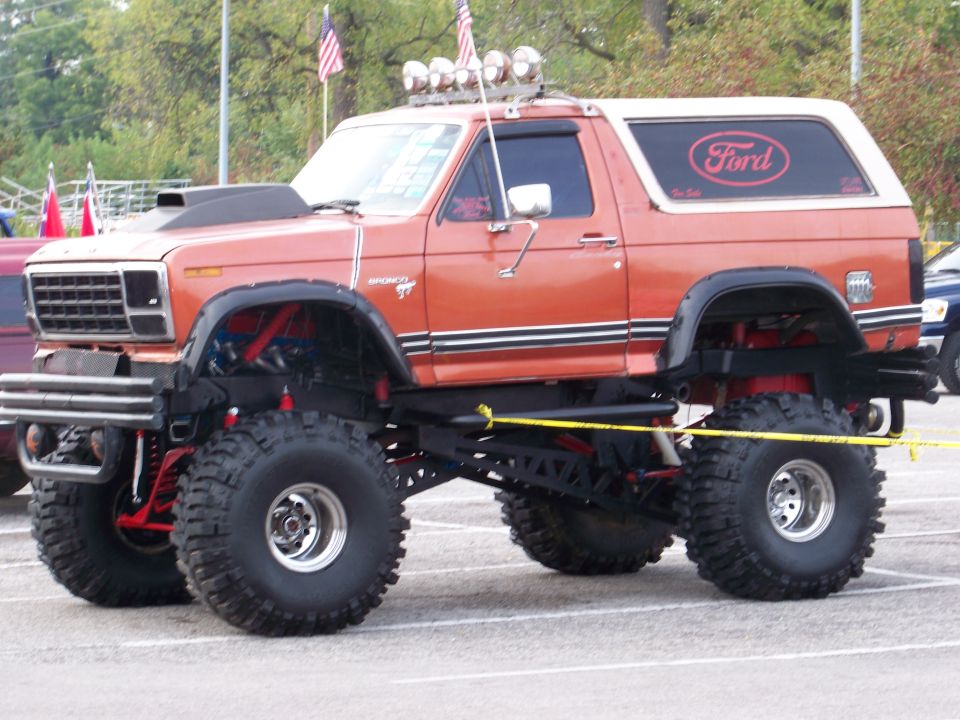 Orange lifted Ford Bronco with big tires and a scoop on the hood. Ford logo on the rear window
