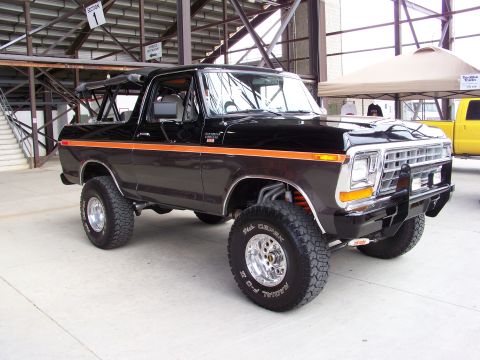 1989 Ford Bronco - This lifted black Ford Bronco is parked indoors next to a yellow truck.