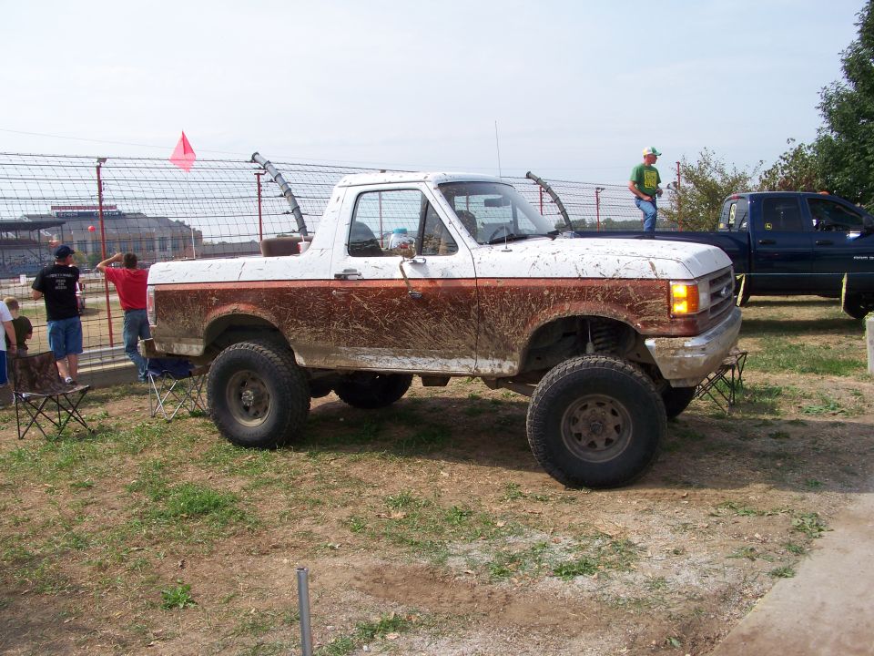 Mud-splattered white and brown Ford Bronco with lifted suspension parked on grass
