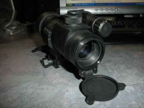 1996 Ford Bronco - A black tactical scope is shown with its lens cap open, resting on a textured surface.