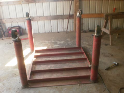 1995 Ford Bronco - A red car lift with four posts and wheels sits on a concrete floor in a workshop.