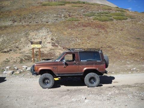 1986 Ford Bronco II - A brown Ford Bronco II is parked on a dirt road near a mountain pass sign.