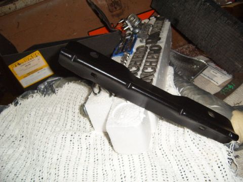 1973 Ford Ranchero - A black metal car part rests on a white textured surface, with "RANCHERO" lettering visible behind it.