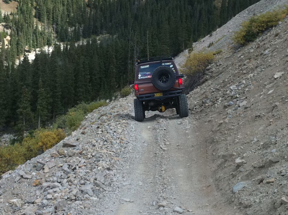 Brown Ford Bronco II driving on a rocky mountain road, rear view