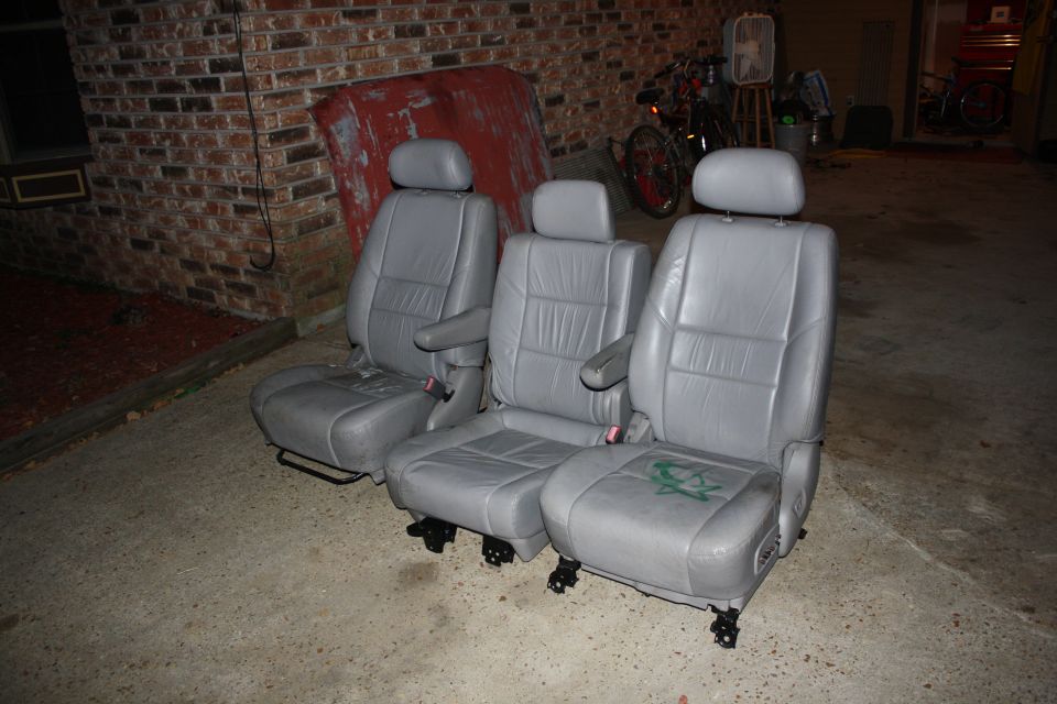 Three gray leather car seats with green graffiti on one seat