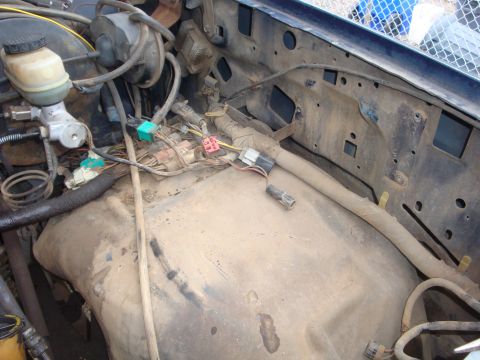 1989 Ford Bronco - A dust-covered empty engine bay with the engine removed, exposing the firewall, inner fenders, a white plastic brake master-cylinder reserv…
