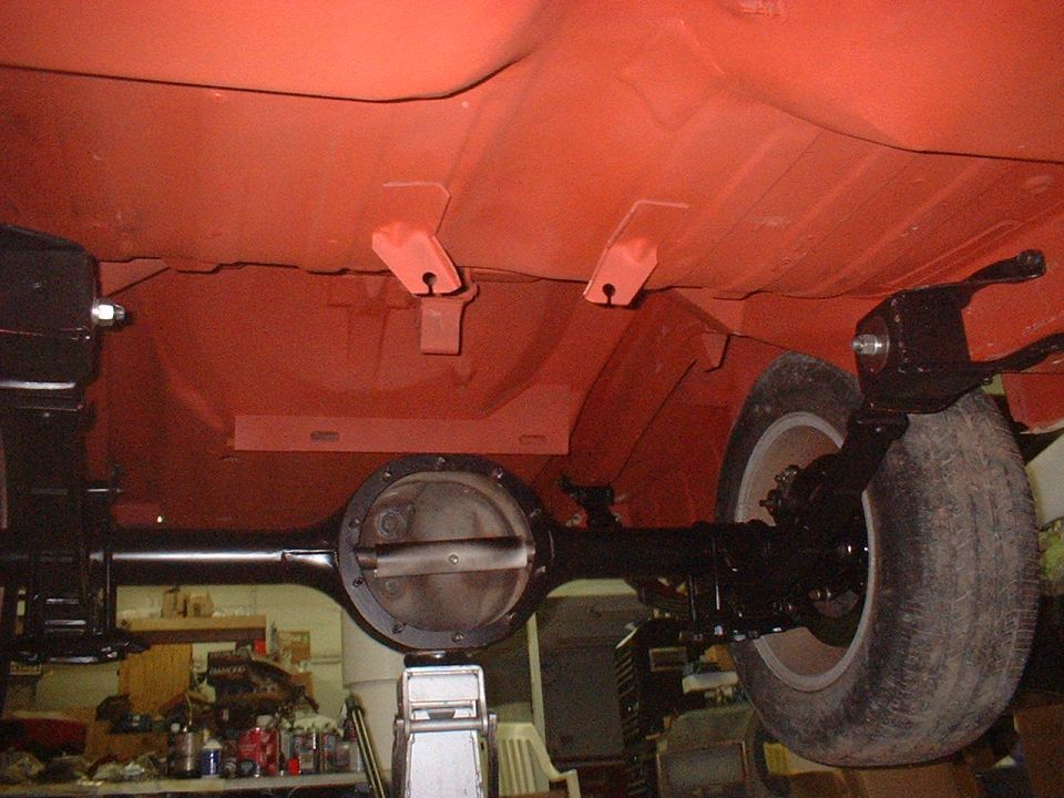 Underside of a car with an orange painted chassis, black differential, and a tire. The vehicle is on a lift in a garage
