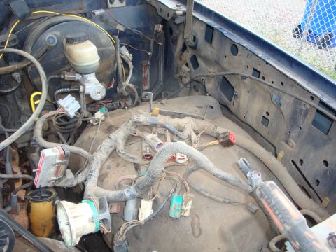 1989 Ford Bronco - Engine bay of a dark blue truck stripped for a swap, with the engine removed and the loose EFI wiring harness laid out across the dusty fir…