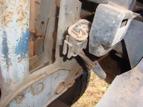 1989 Ford Bronco - Dusty close-up inside an engine bay against a rusty blue-painted inner fender and radiator support, showing a white plastic multi-pin elect…