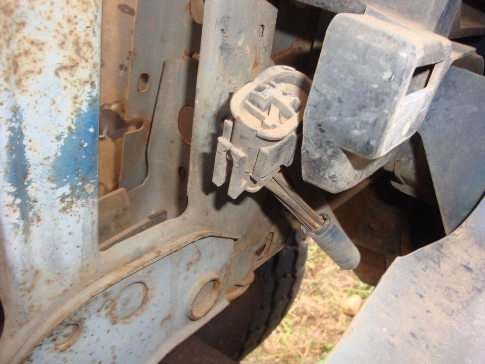 Dusty white plastic electrical connector on bracket beside rusty blue inner fender