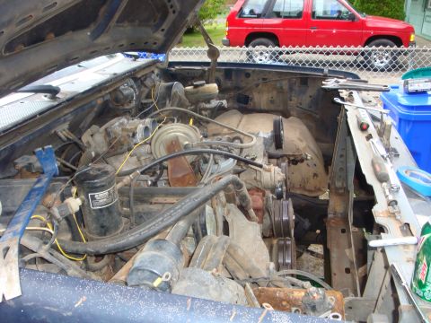 1989 Ford Bronco - The open engine bay of a truck during a V8 engine swap, showing a dusty motor with serpentine pulleys, power-steering pump, oil filter, and…
