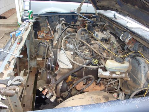 1989 Ford Bronco - Engine bay of a Ford Bronco viewed from the front with the hood open, showing a dusty V8 engine with serpentine belt, spark plug wires, and…