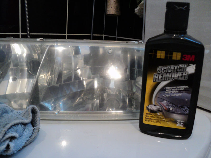 Headlight assembly next to a bottle of 3M scratch remover and a blue cloth