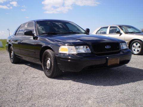 2003 Ford Crown Victoria - A black 2003 Ford Crown Victoria is parked on a gravel lot under a blue sky with clouds.
