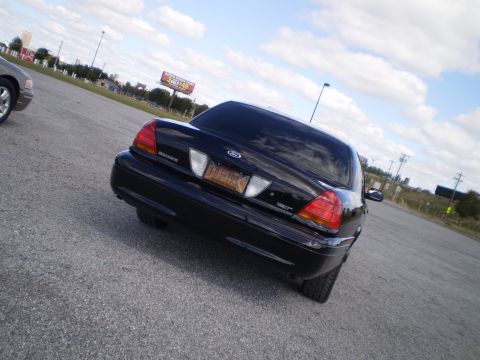 2003 Ford Crown Victoria - A black Ford Crown Victoria is parked on a lot with a billboard in the background.