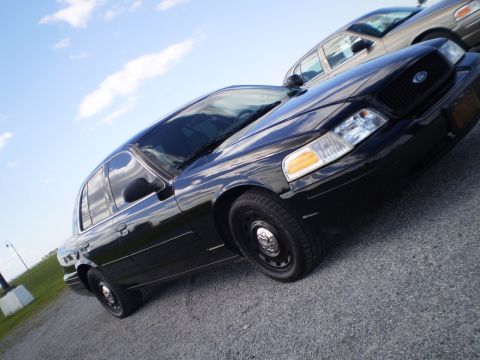 2003 Ford Crown Victoria - A black 2003 Ford Crown Victoria is parked on a gravel lot under a blue sky with clouds.