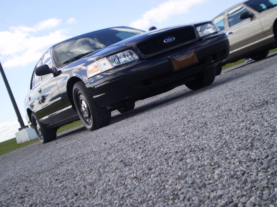 Black 2003 Ford Crown Victoria parked on gravel, another car visible behind it