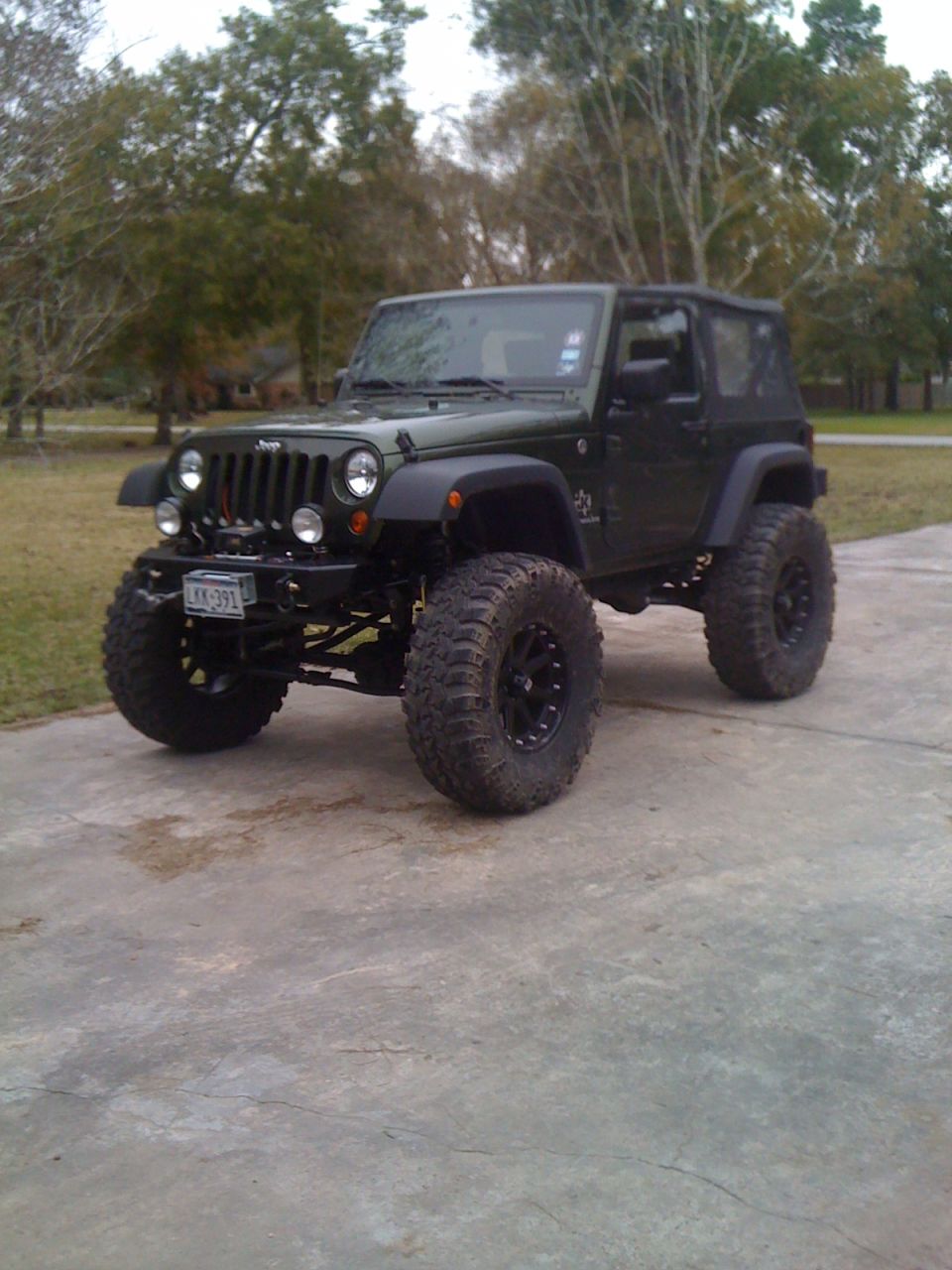 Green Jeep Wrangler with large tires and lifted suspension on a concrete driveway