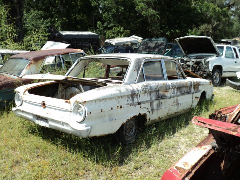1960 Ford Fairlane - This weathered 1960 Ford Fairlane sedan sits in a junkyard, showing signs of significant rust and decay.