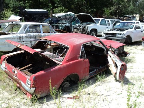 1960 Ford Fairlane - This red coupe, likely a 1965 model, is in a junkyard with its doors and trunk open.