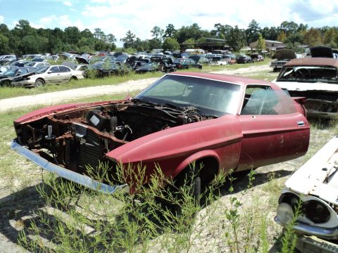 1960 Ford Fairlane - A red coupe sits in a junkyard, its front end dismantled and engine missing.