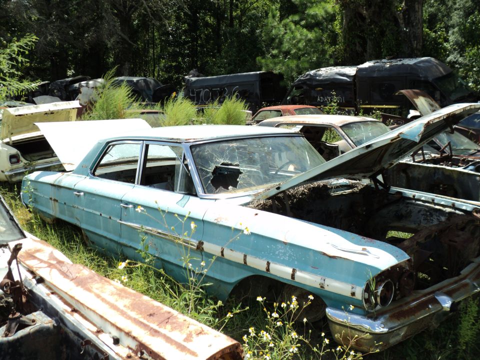 Light blue 1961 sedan with a broken windshield and white trim, parked in a junkyard