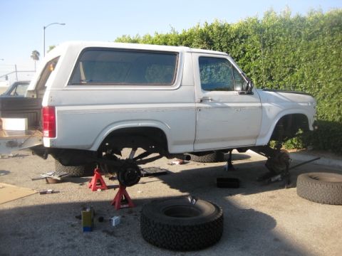 1986 Ford Bronco - White SUV on jack stands with wheels removed, showing its undercarriage and suspension system.