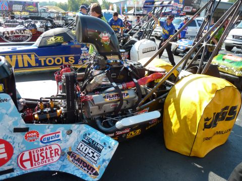 1992 Ford Mustang - A drag racing car's powerful engine is detailed with sponsor logos, parked at a track with other vehicles.