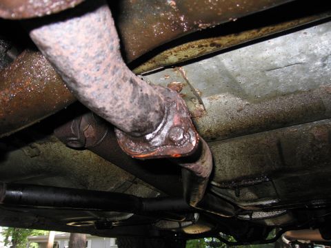 1991 Ford LTD Crown Victoria - Close-up of a corroded exhaust pipe joint underneath a vehicle.