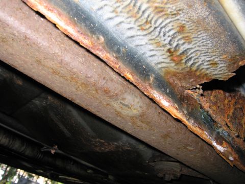 1991 Ford LTD Crown Victoria - The undercarriage of a vehicle shows significant rust damage on the frame and exhaust components.