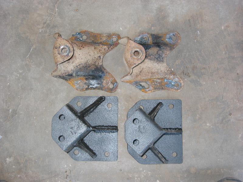 Two rusty stock brackets above two black reinforced replacement bracket plates on concrete floor