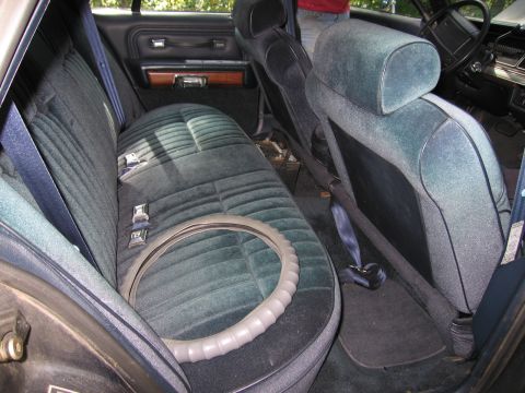 1991 Ford LTD Crown Victoria - The interior of a car, plush velour seats and seatbelts, with a steering wheel cover resting on the back seat.