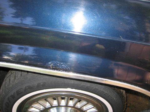 1991 Ford LTD Crown Victoria - Close-up of a blue car's side panel showing a rust patch and a portion of the wheel.