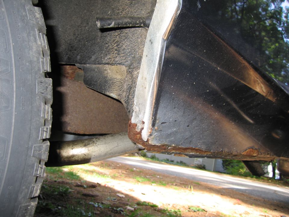 Close-up of a car's rear fender showing rust, with a tire and exhaust pipe visible