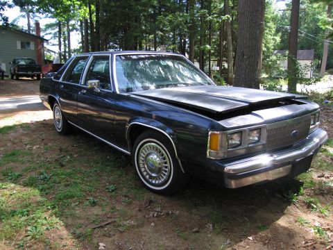 1991 Ford LTD Crown Victoria - Dark blue 1991 Ford Crown Victoria LTD sedan with hood ajar, parked outdoors.