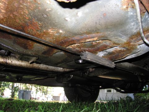 1991 Ford LTD Crown Victoria - Heavily rusted undercarriage of a car, showing brake lines and suspension parts.