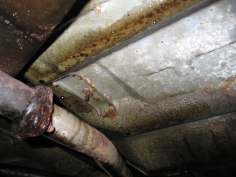 1991 Ford LTD Crown Victoria - The underside of a vehicle displays significant rust on its exhaust system and frame components.