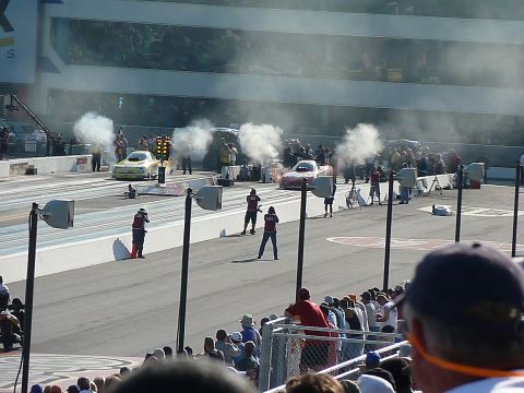 1992 Ford Mustang - Drag racing cars prepare for a race, with smoke billowing from their tires and a crowd watching.