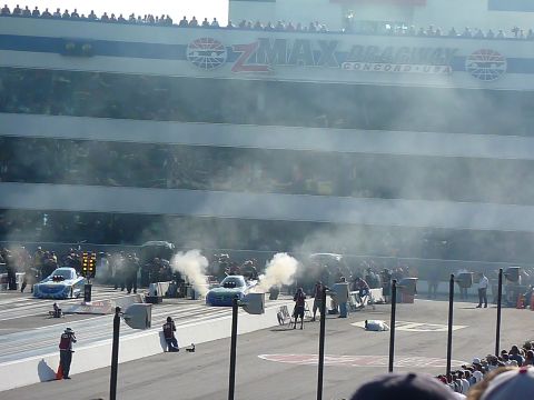 1992 Ford Mustang - Two dragsters prepare for a race at ZMAX Dragway, generating smoke as crowds watch from the stands.