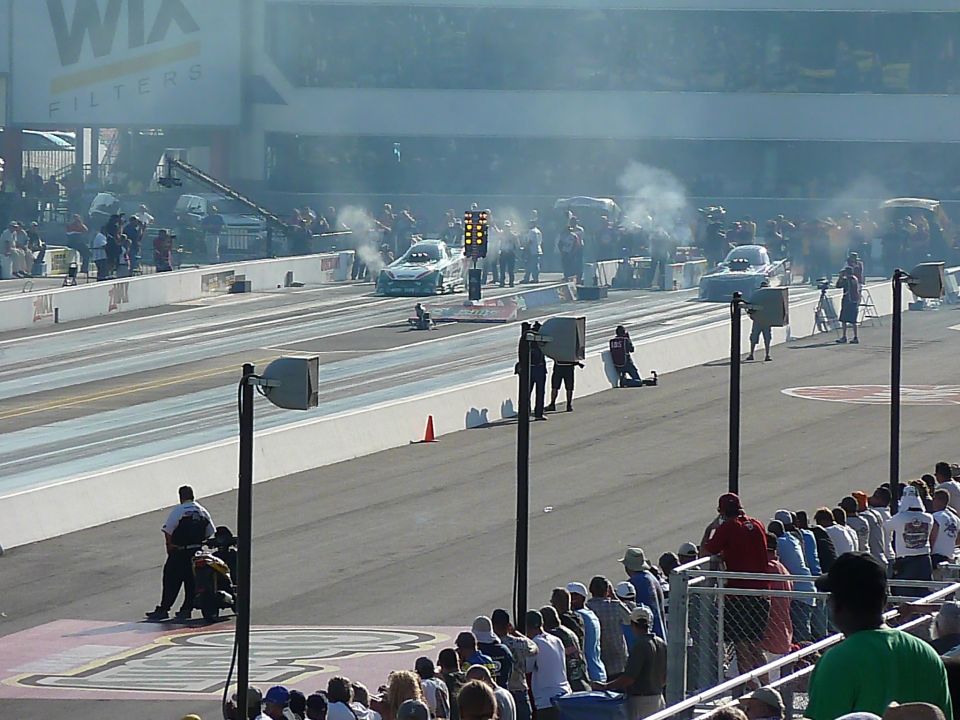 Two drag cars at the starting line, smoke coming from tires, crowd watching