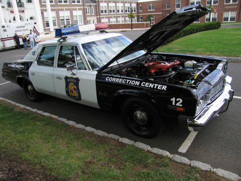 1991 Ford LTD Crown Victoria - black and white vintage sedan lettered 'Correction Center' and 'Essex' number 12 with hood raised, parked outside brick buildings.