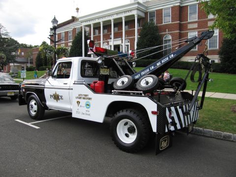 1991 Ford LTD Crown Victoria - black-and-white Ford police tow truck fitted with a wrecker boom and POLICE markings parked outside a building.