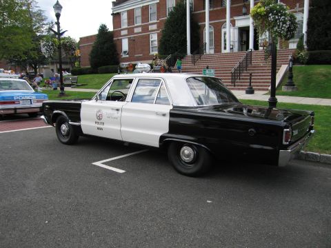 1991 Ford LTD Crown Victoria - black-and-white police sedan with a single red roof light and door shield parked at a curb by a brick building.