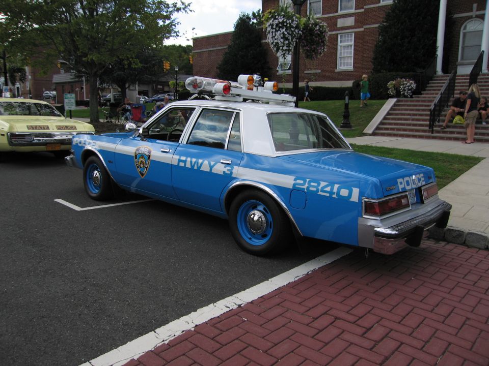 Blue and white NYPD-style police sedan with HWY light bar, rear three-quarter view
