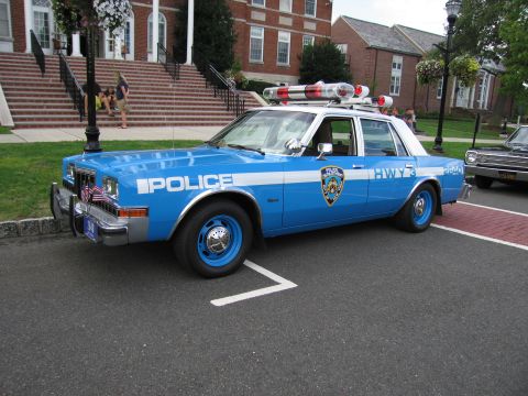 1991 Ford LTD Crown Victoria - blue-and-white police sedan marked POLICE and HWY 3 with blue wheels and a roof light bar parked at a curb.