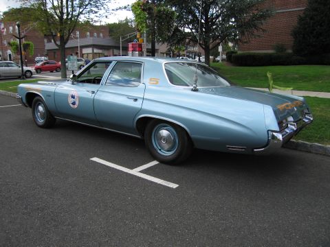 1991 Ford LTD Crown Victoria - light blue full-size police sedan with a round door decal and the number 5 on the roof parked at a curb.